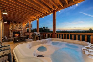 A hot tub with a stone fireplace, wooden deck, and a view of the landscape.