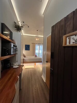 A modern kitchen with a microwave, oven, and coffee maker. A bed with a white comforter is visible in the background. - #1 Queen Bed, Beach 1 min, St. Lawrence Gap (Oistins)