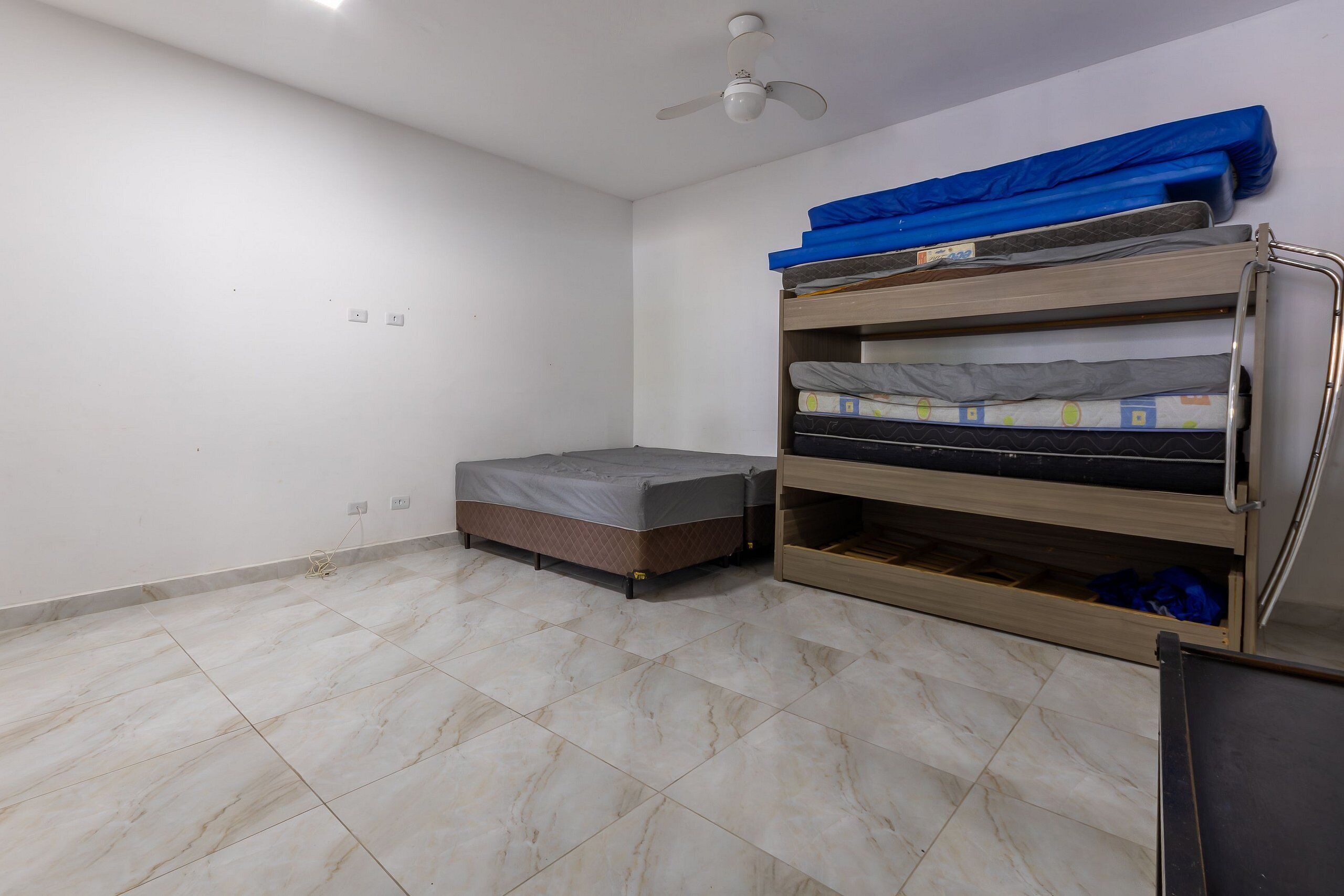 Um quarto com beliche, cama de solteiro e ventoinha no teto.