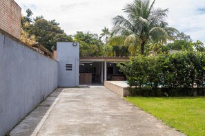 A pathway leading to a building with a covered entrance, surrounded by greenery and a palm tree. - Casa  piscina a 180m da Praia Boraceia (Bertioga)