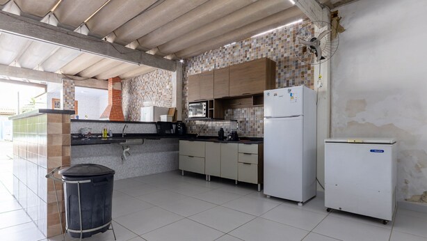 A kitchen with tiled flooring, a trash bin, a microwave, and a refrigerator. - Casa  piscina a 180m da Praia Boraceia (Bertioga)