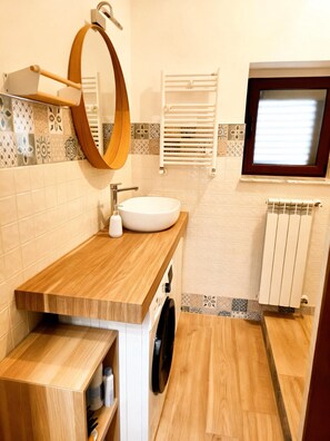 A bathroom with a wooden vanity, a round mirror, a white sink, a towel rack, and a window. - Detached house in the center near the sea and the Spa Center (Margherita di Savoia)