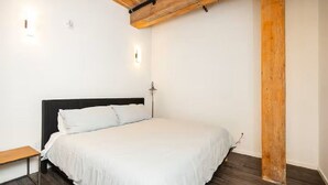 Une chambre avec une poutre en bois au plafond, un lit avec une literie blanche et une table de chevet.