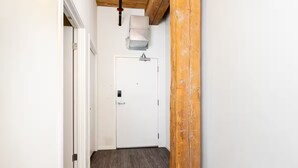 Un couloir avec un plafond en bois, une porte blanche dotée d’une poignée et un tapis noir sur le sol.