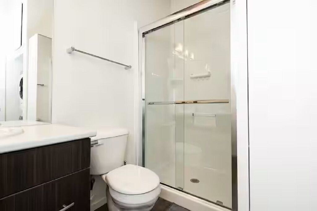 A bathroom with a glass shower enclosure, a white toilet, and a dark wood vanity.