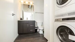Une petite salle de bain avec un meuble-lavabo en bois foncé, des toilettes blanches et un lave-linge à chargement frontal.