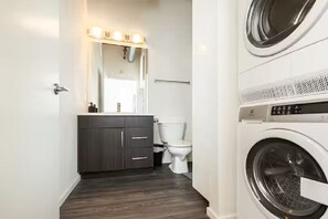 Une petite salle de bain avec un meuble-lavabo en bois foncé, des toilettes blanches et un lave-linge à chargement frontal.