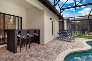 Eine Terrasse mit Pool, ein Barbereich mit Stühlen und ein überdachter Sitzbereich.