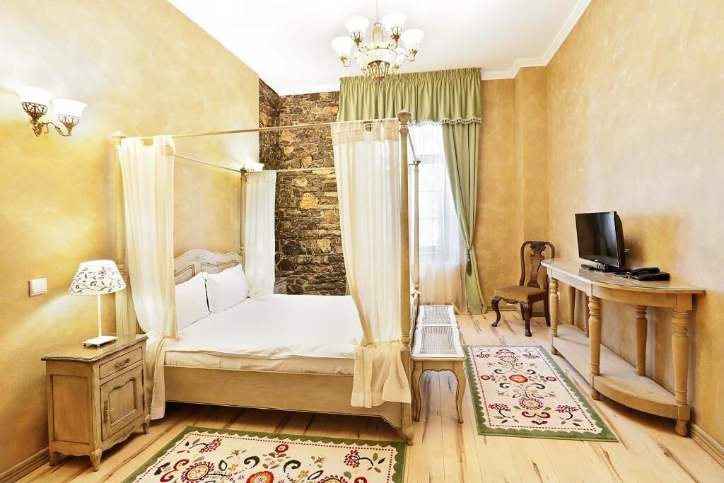 A bedroom with a four-poster bed, a stone wall, a television on a wooden console, and a small table with a lamp.
