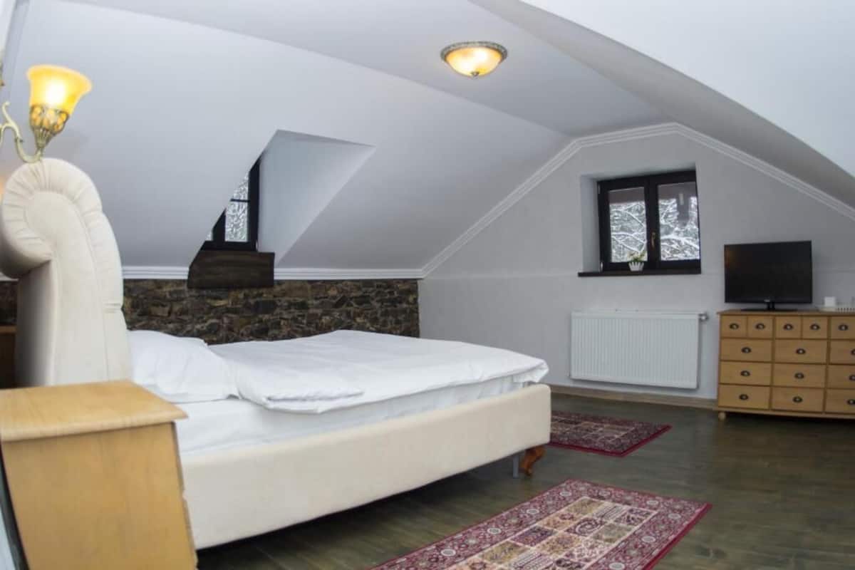 A bedroom with a bed, a dresser, a television, a window, and a stone wall.