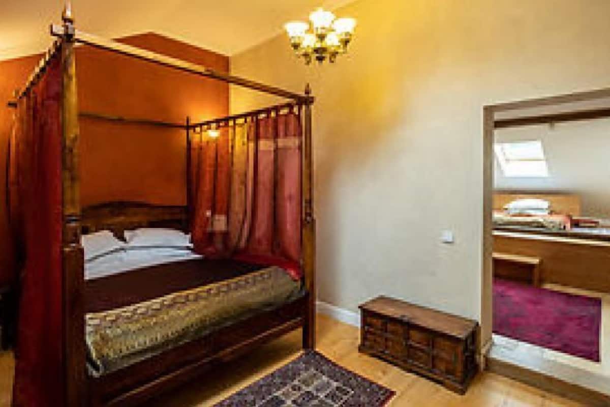 A four-poster bed with a wooden headboard, a nightstand, a bedside table, and a window with a view.