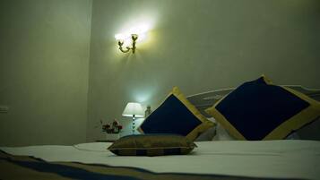 A hotel room with a bed, pillows, a nightstand with a lamp, and a wall-mounted light fixture.