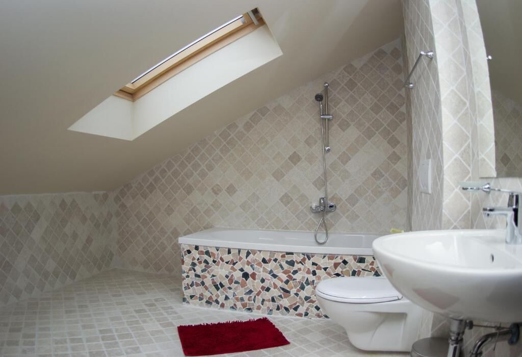 A bathroom with a skylight, a bathtub, a toilet, and a sink.