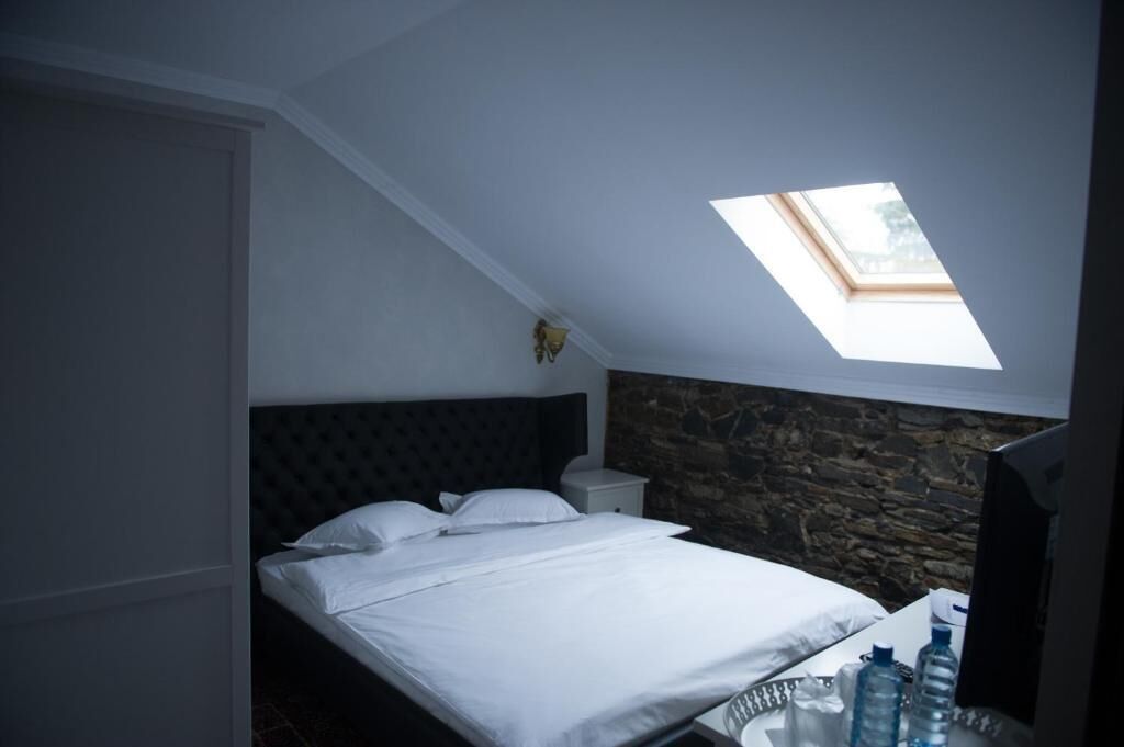 A bedroom with a bed, a nightstand, a stone wall, and a skylight.