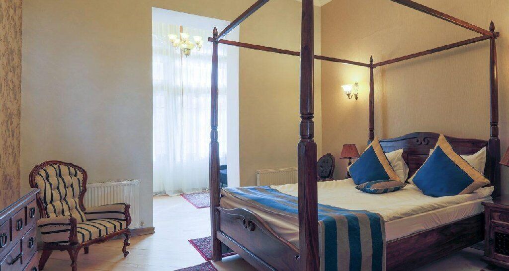 Una cama con dosel de madera, una silla con estampado a rayas y un radiador en la pared.