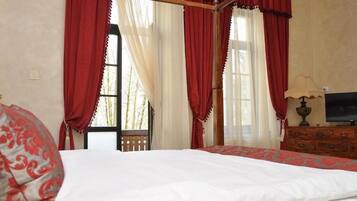 Une chambre à coucher avec un lit à baldaquin, un téléviseur posé sur une commode en bois et une fenêtre ornée de rideaux rouges.