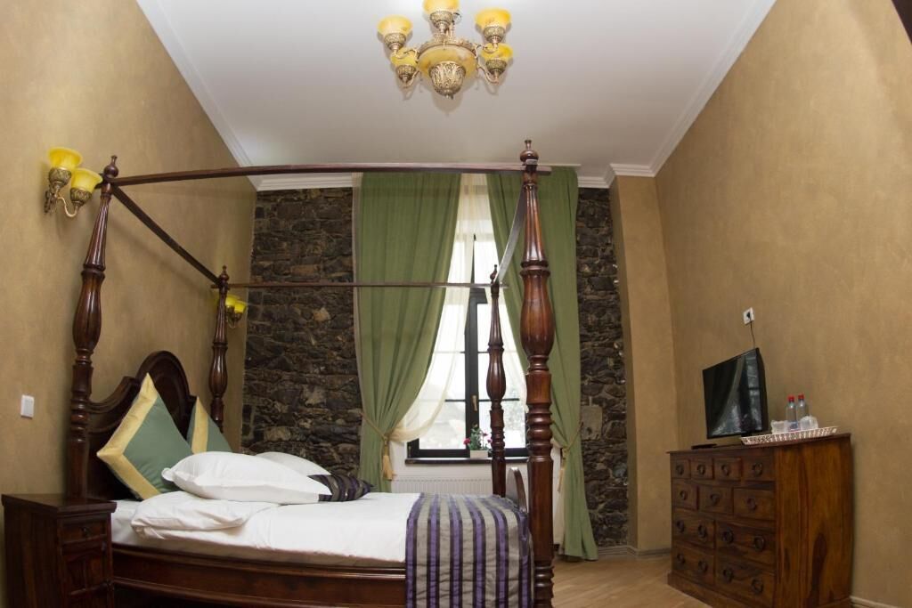 A bedroom with a four-poster bed, a stone wall, a green curtain, a wooden dresser, and a television on the dresser.