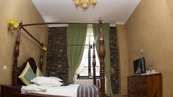 A bedroom with a four-poster bed, a stone wall, a green curtain, a wooden dresser, and a television on the dresser.