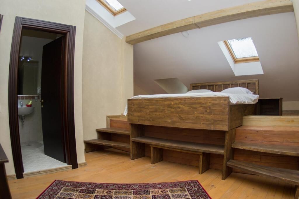 A bedroom with a wooden bed, skylights, a bathroom with a sink, and a patterned rug.