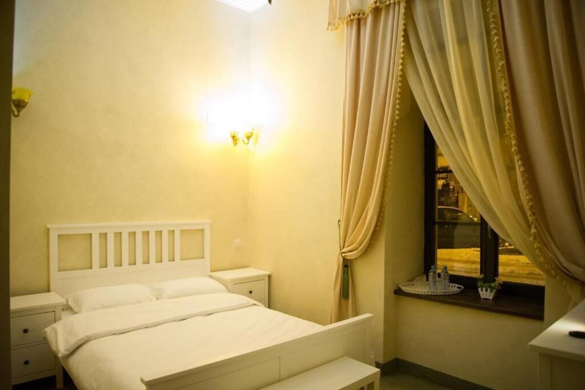 A bedroom with a bed, bedside tables, a window with curtains, and wall-mounted lights.