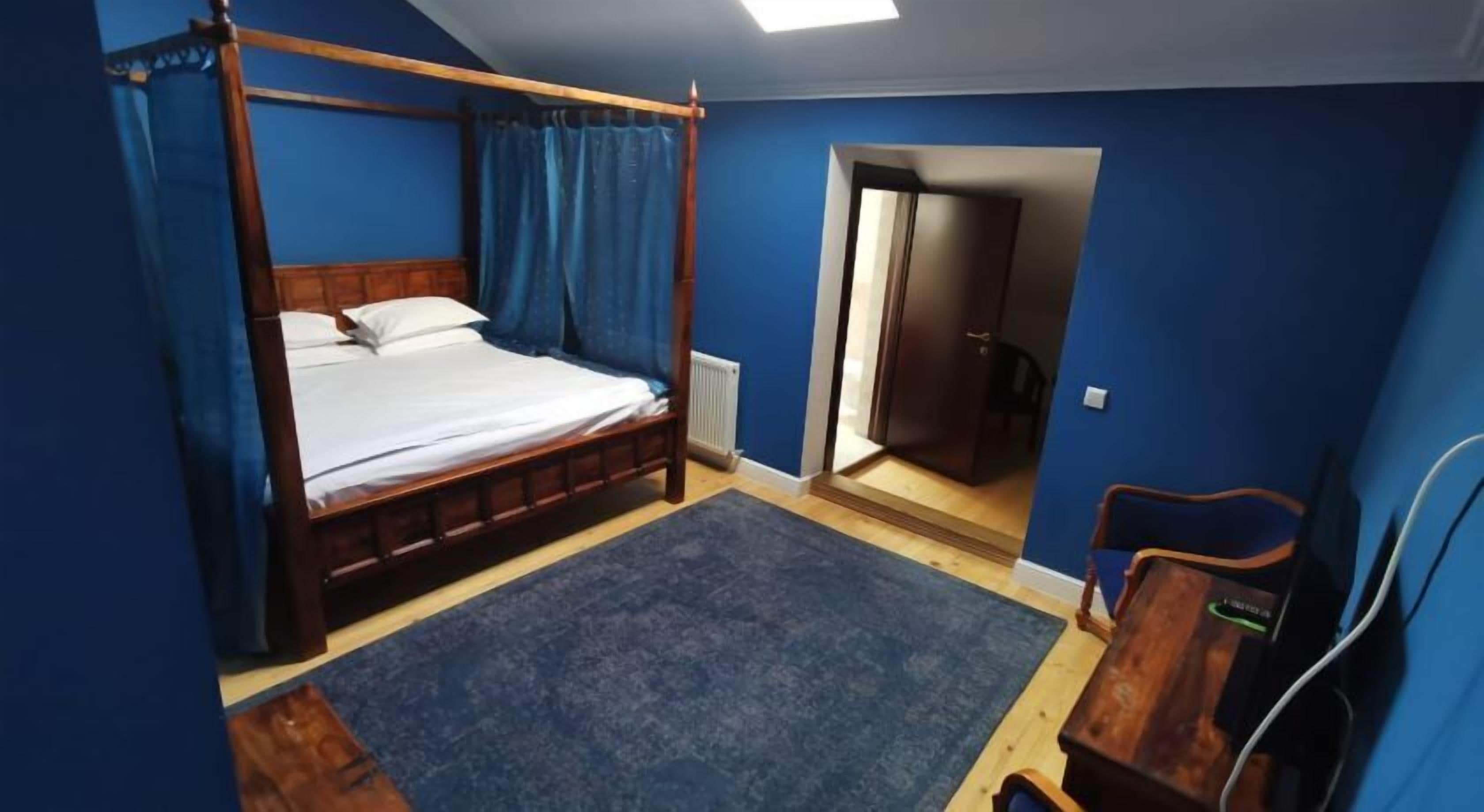 A bedroom with a four-poster bed, a blue carpet, and a wooden dresser.