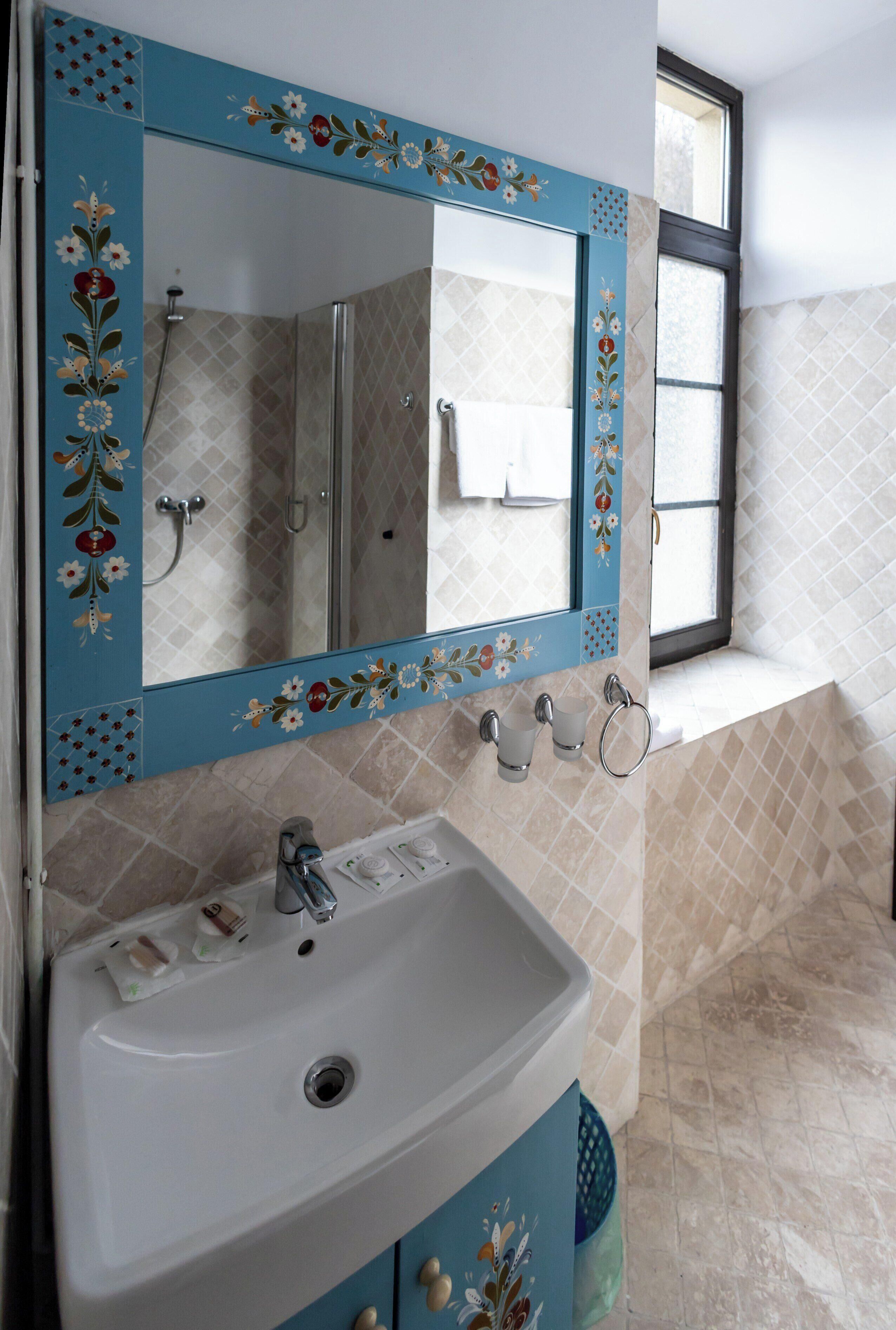 A bathroom with a white sink, a mirror with floral designs, and a window.