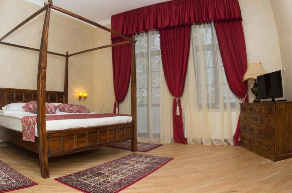 Un lit à baldaquin avec un cadre en bois, une commode en bois dotée de nombreux tiroirs et une grande fenêtre ornée de rideaux rouges.