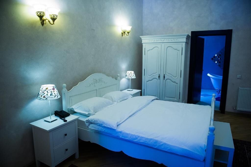 A bedroom with a bed, nightstands, a wardrobe, and wall sconces.