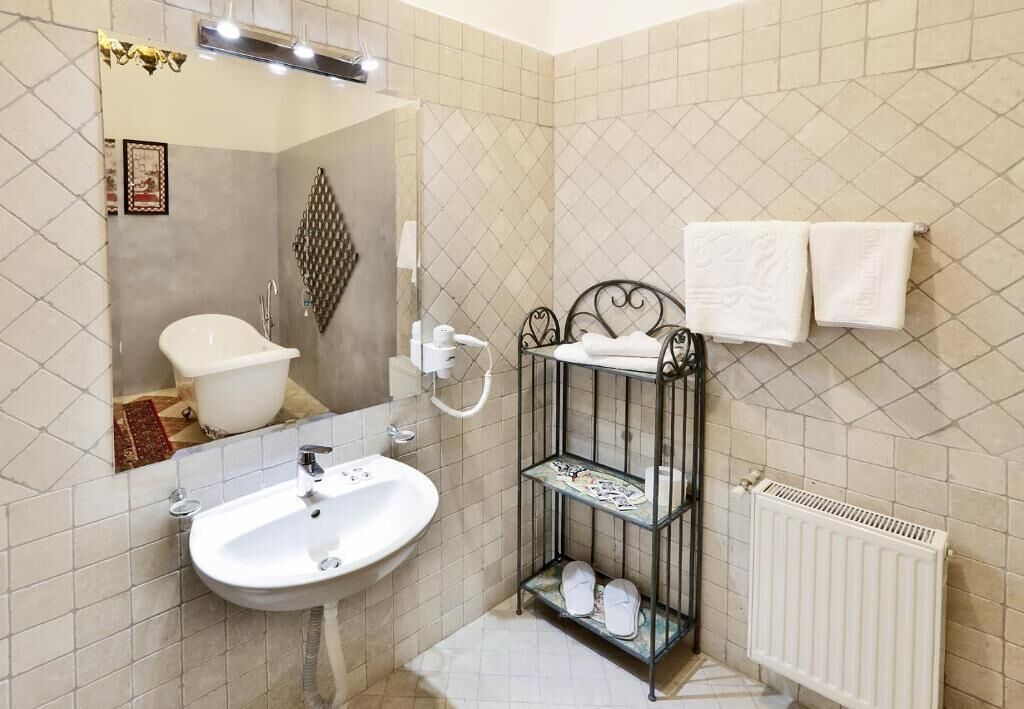 Un baño con lavamanos blanco, bañera, espejo, radiador y estante con toallas.