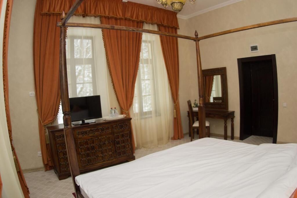 A bedroom with a four-poster bed, a wooden dresser, a television, and a mirror.
