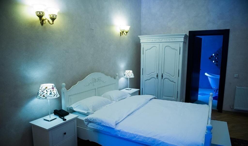 Une chambre à coucher avec un lit, des tables de chevet, une lampe, une armoire et une salle de bain visible à travers une porte ouverte.