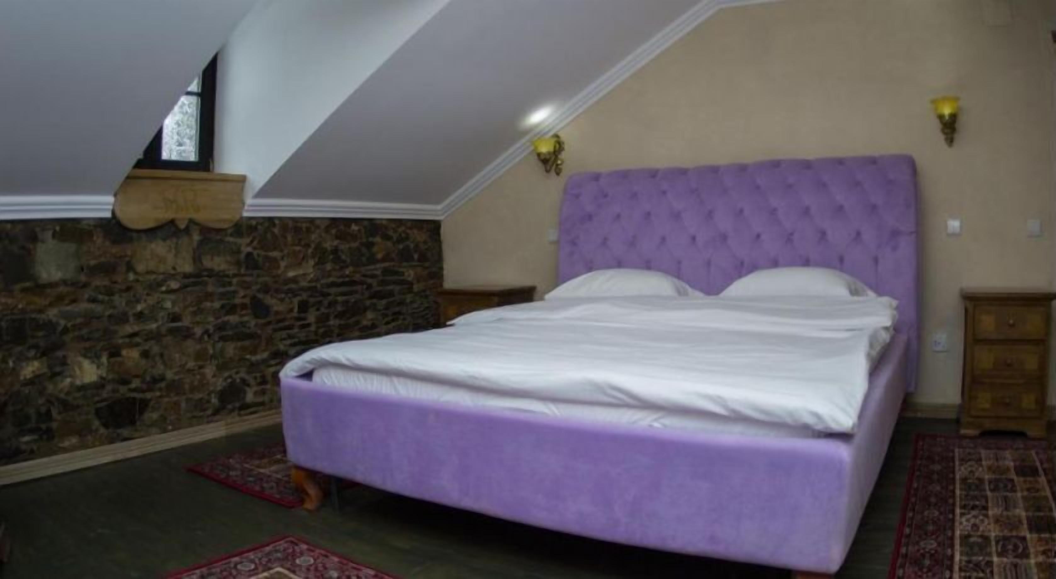 A bedroom with a stone wall, a purple bed, and a sloped ceiling.
