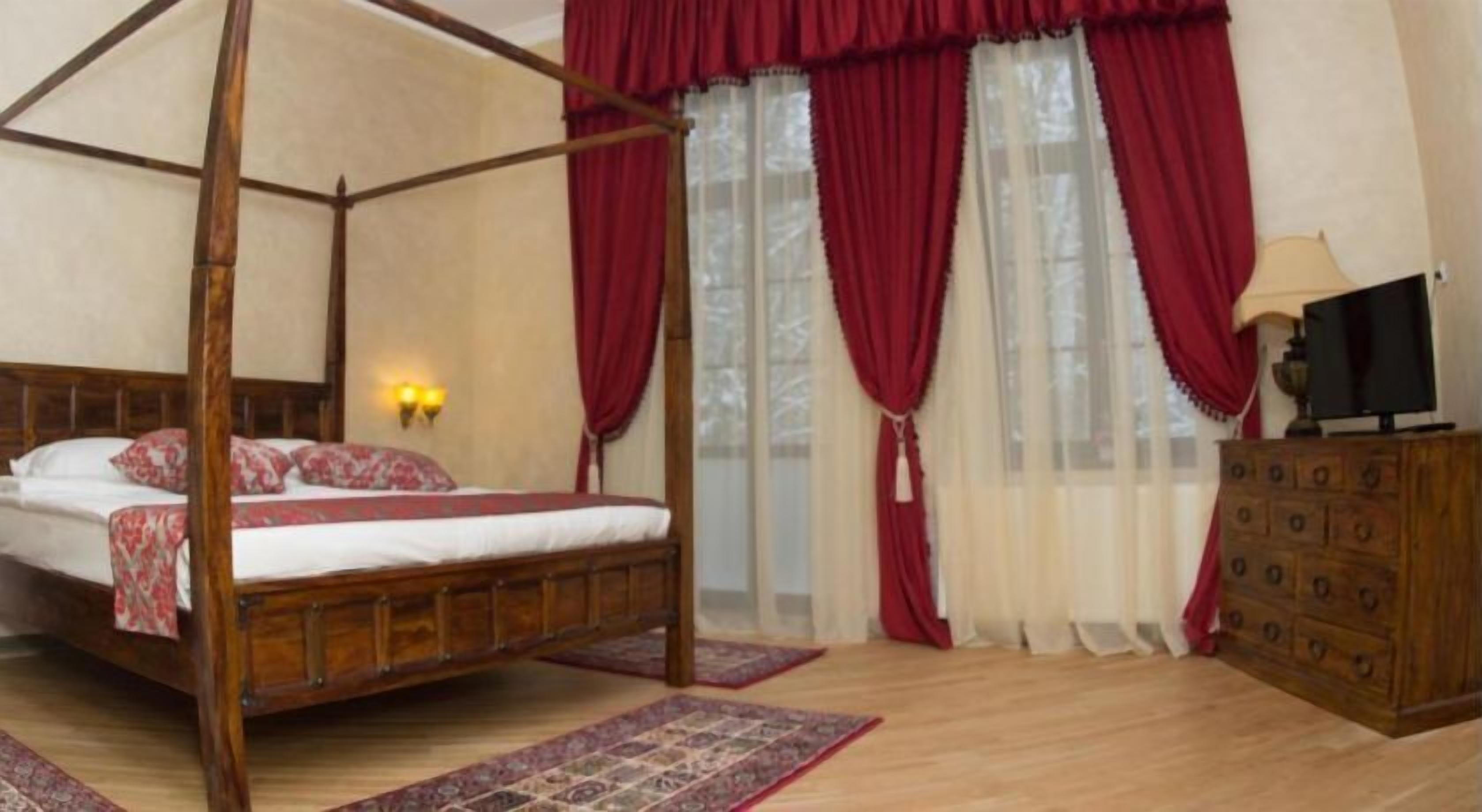 Una cama con dosel y tablero de madera, un aparador de madera con varios cajones, y un televisor encima.
