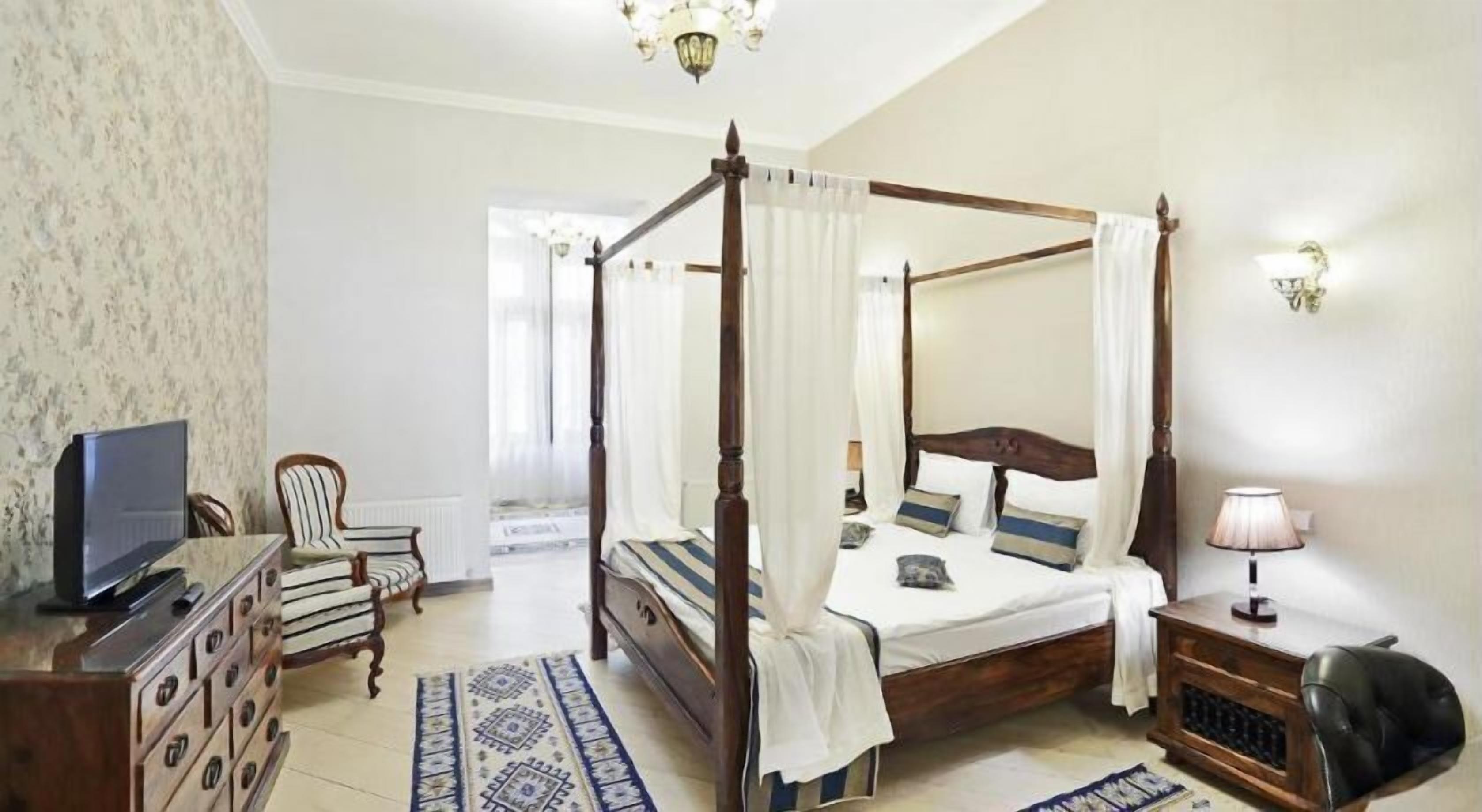 A four-poster bed with a canopy, a television on a dresser, a chair, and a lamp.