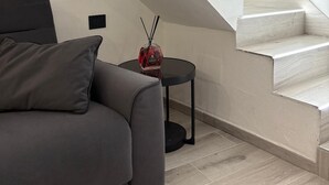 Ein modernes Wohnzimmer mit einem grauen Sofa, einem kleinen runden Tisch mit einer roten Flasche und einer Treppe mit weißen Stufen.