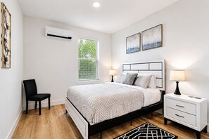 Un dormitorio moderno con cama, mesitas de noche, una silla y obras de arte.