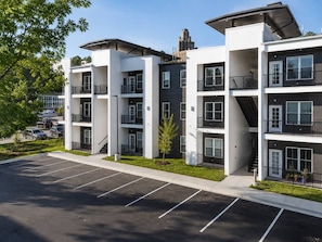 A multi-story residential building with balconies, a parking lot, and a clear sky. - Inviting Downtown Suite • 1BR • Free Parking (Hot Springs)