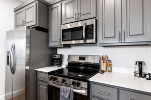 A modern kitchen with stainless steel appliances, grey cabinetry, and a black stove. - Inviting Downtown Suite • 1BR • Free Parking (Hot Springs)