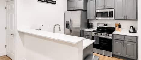 Una cocina moderna con gabinetes grises, electrodomésticos de acero inoxidable y encimera blanca.