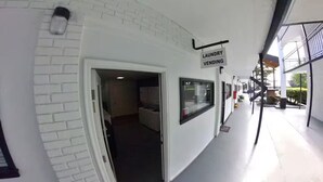 A corridor with a laundry vending sign, a white brick wall, and a window with a view of the outside. - The Urban Oasis (Cleveland)
