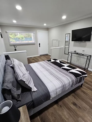Ein modernes Schlafzimmer mit einem großen Bett, einem Fernseher und einem Fenster mit Jalousien.