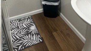 A bathroom with a white sink, a black trash bin, a patterned rug, and wooden flooring.