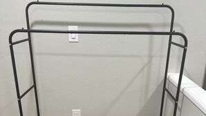 A metal drying rack with a white wall and wooden flooring.