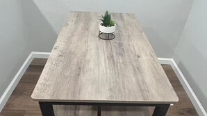 A rectangular dining table with a light wood finish, black metal legs, and a small potted plant on top.