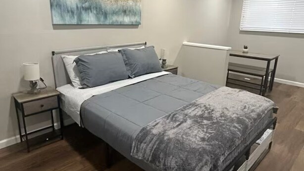 A bedroom with a bed, nightstands, a wall art piece, and a window with blinds.