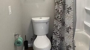 Een badkamer met een toilet, een plank met handdoeken, een douchegordijn en een toiletborstel.