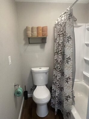 A bathroom with a toilet, a shelf with towels, a shower curtain, and a toilet brush. - The Orange Sunset (Cleveland)