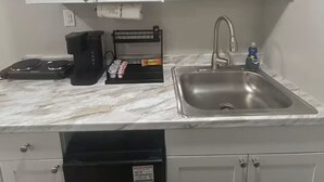 Een kleine keuken met witte kastjes, een magnetron, een koffiezetapparaat, een spoelbak en een vaatwasser.
