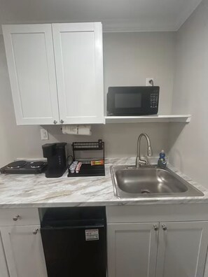 A compact kitchen with white cabinets, a microwave, a coffee maker, a sink, and a dishwasher. - The Orange Sunset (Cleveland)