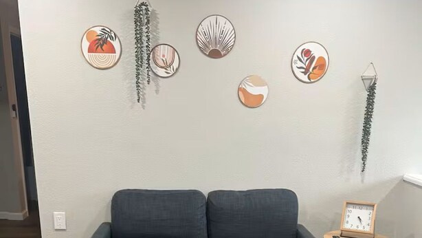 Een woonkamer met een donkergrijze bank, een glazen salontafel en een kamerbreed tapijt met patroon.